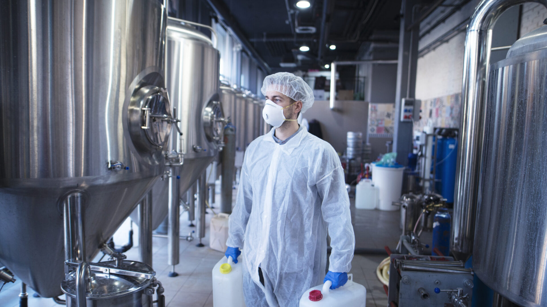 Technologist industrial worker holding plastic canisters about to change chemicals in the food processing machine.